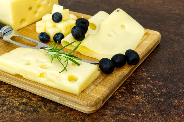 Skivad ost med oliver och rosmarin på en träskiva. Förrätt av vinost — Stockfoto