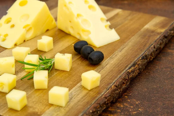 Skivad ost med oliver och rosmarin på en träskiva. Förrätt av vinost — Stockfoto
