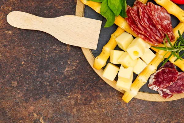 Snack antipasti de carne y queso con jamón Prosciutto, parmesano, queso azul, melón cantalupo y aceitunas sobre tabla de servir de madera de olivo sobre fondo de piedra oscura — Foto de Stock