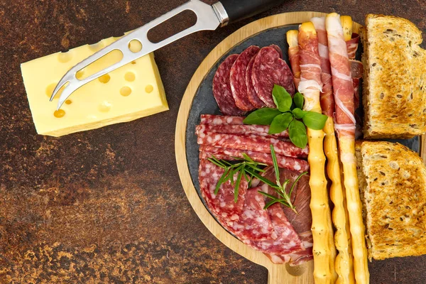 Snack antipasti de carne y queso con jamón Prosciutto, parmesano, queso azul, melón cantalupo y aceitunas sobre tabla de servir de madera de olivo sobre fondo de piedra oscura — Foto de Stock