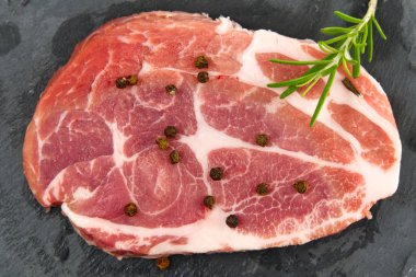 Siyah taş ve ahşap üzerinde çiğ domuz eti. Baharatlı domuz eti: biberiye ve biber. Yakın plan çiğ domuz bifteği..