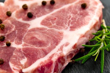 Siyah taş ve ahşap üzerinde çiğ domuz eti. Baharatlı domuz eti: biberiye ve biber. Yakın plan çiğ domuz bifteği..