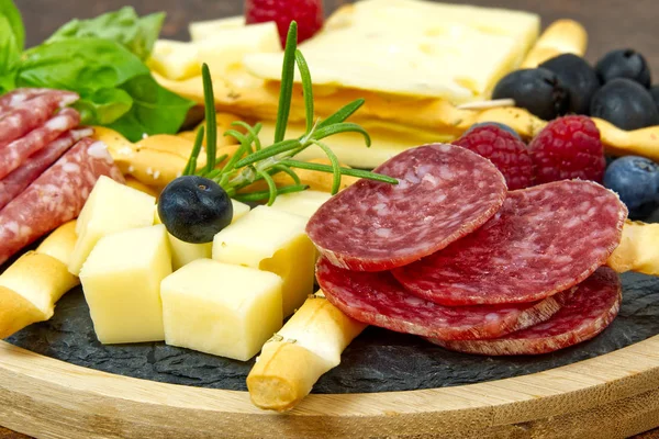 Snack antipasti de carne y queso con jamón Prosciutto, parmesano, queso azul, melón cantalupo y aceitunas sobre tabla de servir de madera de olivo sobre fondo de piedra oscura — Foto de Stock