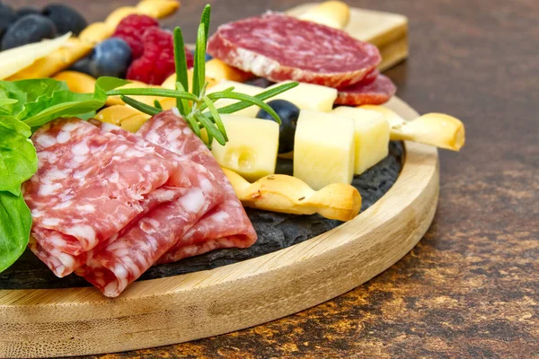 Snack antipasti de carne y queso con jamón Prosciutto, parmesano, queso azul, melón cantalupo y aceitunas sobre tabla de servir de madera de olivo sobre fondo de piedra oscura — Foto de Stock