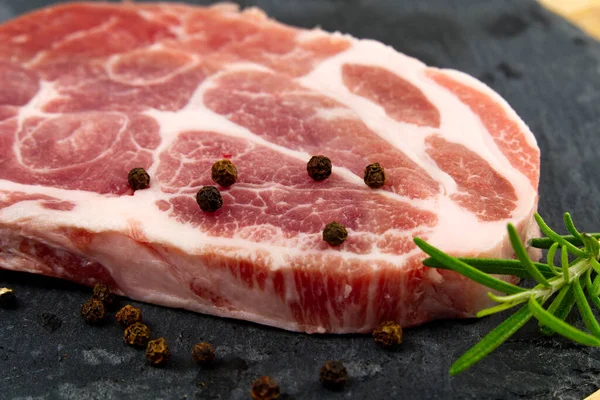 Bife de porco cru em pedra preta e madeira. Porco com temperos: alecrim e pimentão. Bifes de porco crus close-up . — Fotografia de Stock