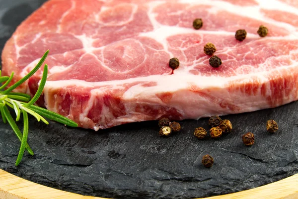 Raw pork steak on black stone and wood. Pork with spices: rosemary and pepper. Close-up raw pork steaks. — Stock Photo, Image