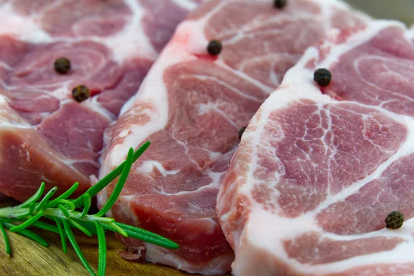 Bife de porco cru na placa de corte de madeira. Porco com temperos: alecrim e pimentão. Bifes de porco crus close-up . — Fotografia de Stock