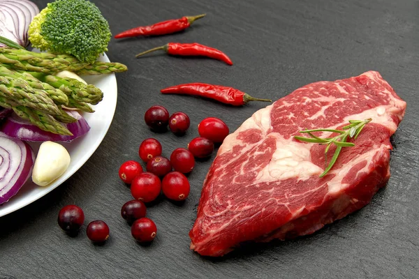 Baharatlı ve sebzeli çiğ biftek. Restoran yemeği için gerekli malzemeler. Taze et, tuz, biberiye, kekik, biber, kiraz domatesleri, siyah taşta sarımsak. Gıda arkaplanı. — Stok fotoğraf