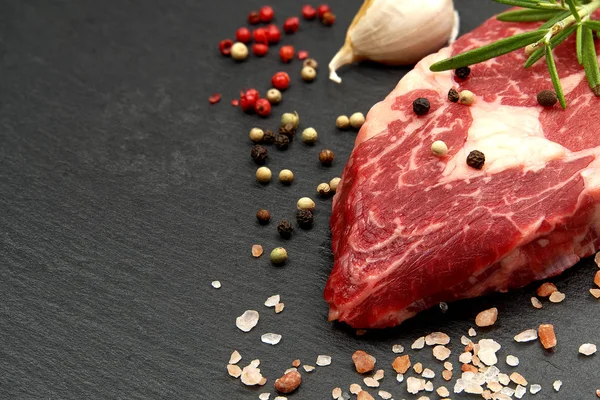 Syrový žebírkový steak s kořením a zeleninou. Ingredience na jídlo z restaurace. Čerstvé maso, sůl, rozmarýn, tymián, chilli, cherry rajčata, česnek na černém kameni. Pozadí potravin. — Stock fotografie