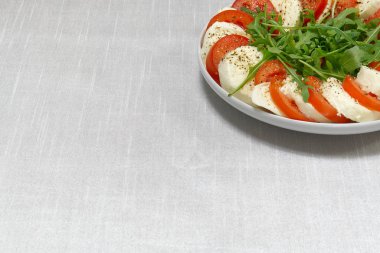 Masada mozzarella, domates ve roka dilimleri var. Mozzarella ve domates, metin için bir tabağa konmuş..