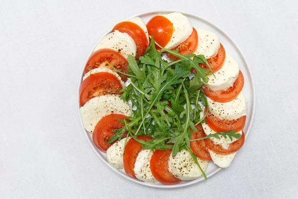 Rebanadas de mozzarella, tomates y rúcula sobre la mesa. Mozzarella y tomate apilados en un plato con lugar para texto . —  Fotos de Stock