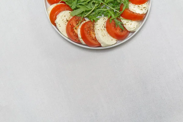 Rebanadas de mozzarella, tomates y rúcula sobre la mesa. Mozzarella y tomate apilados en un plato con lugar para texto . —  Fotos de Stock