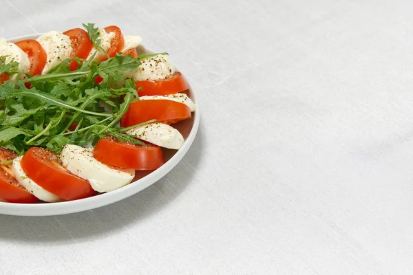 Rebanadas de mozzarella, tomates y rúcula sobre la mesa. Mozzarella y tomate apilados en un plato con lugar para texto . —  Fotos de Stock