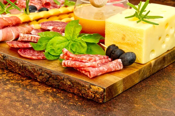 Snack antipasti de carne y queso con jamón Prosciutto, parmesano, queso azul, melón cantalupo y aceitunas sobre tabla de servir de madera de olivo sobre fondo de piedra oscura — Foto de Stock