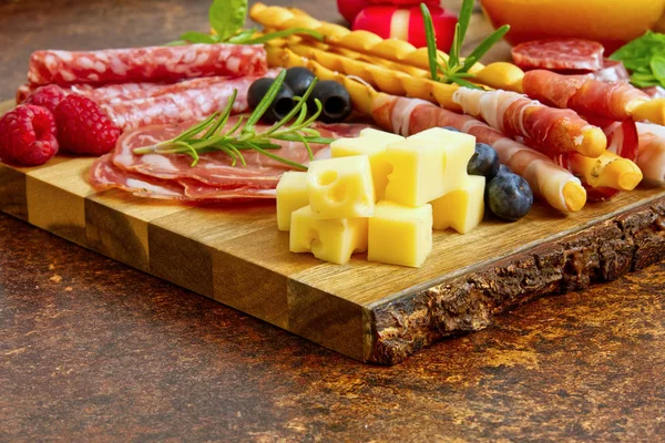 Snack antipasti de carne y queso con jamón Prosciutto, parmesano, queso azul, melón cantalupo y aceitunas sobre tabla de servir de madera de olivo sobre fondo de piedra oscura — Foto de Stock