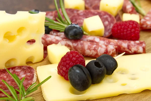 Snack antipasti de carne y queso con jamón Prosciutto, parmesano, queso azul, melón cantalupo y aceitunas sobre tabla de servir de madera de olivo sobre fondo de piedra oscura — Foto de Stock