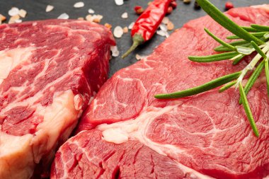 Baharatlı ve sebzeli çiğ biftek. Restoran yemeği için gerekli malzemeler. Taze et, tuz, biberiye, kekik, biber, kiraz domatesleri, siyah taşta sarımsak. Gıda arkaplanı.