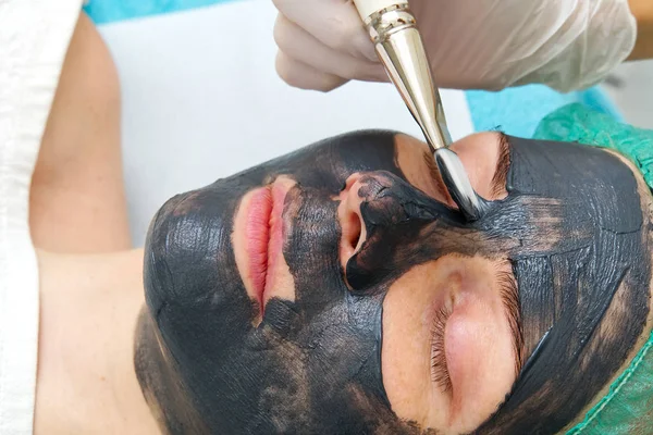 Косметик наносит натуральную увлажняющую маску на лицо молодой красивой женщины. Черный бамбук Угольная маска для лица, нанесенная на лицо кистью . — стоковое фото