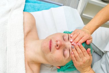 Güzellik uzmanı genç ve güzel bir kadının yüzüne doğal nemlendirici bir maske takar. Yaşlanma önleyici maske ve sorunlu cilt kırışıklıkları. Kozmetoloji konsepti. Kozmetik uzmanı ameliyatı...