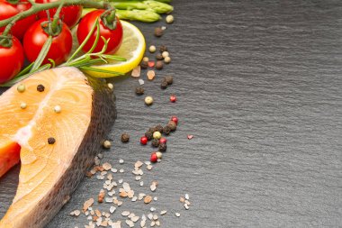 siyah arka plan üzerinde biber mısır, tuz, limon ve zeytinyağı ile taze çiğ somon biftek. Sağlıklı gıda, diyet konsepti. Baharatlı balık pişirmeye hazırlık