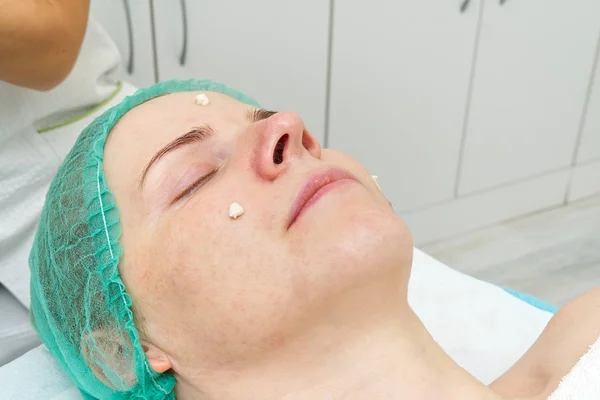 Beautician applicerar en naturlig fuktgivande mask på ansiktet av en ung vacker kvinna. Anti-aging mask och rynkor för problemhud. Kosmetologiskt koncept. Kosmetologen utför proceduren att — Stockfoto