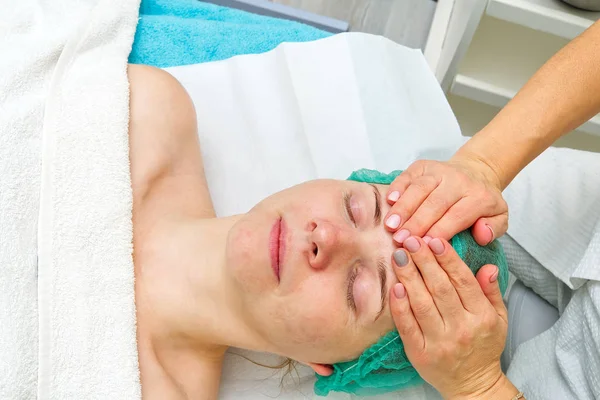 Beautician applicerar en naturlig fuktgivande mask på ansiktet av en ung vacker kvinna. Anti-aging mask och rynkor för problemhud. Kosmetologiskt koncept. Kosmetologen utför proceduren att — Stockfoto