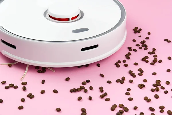 Aspirator robot alb pe un fundal roz cu boabe de cafea. Conceptul de curățare cu un robot curat — Fotografie, imagine de stoc