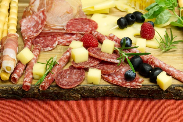 Snack antipasti de carne y queso con jamón Prosciutto, parmesano, queso azul, melón melón y aceitunas sobre tabla de servir de madera de olivo sobre fondo rojo — Foto de Stock