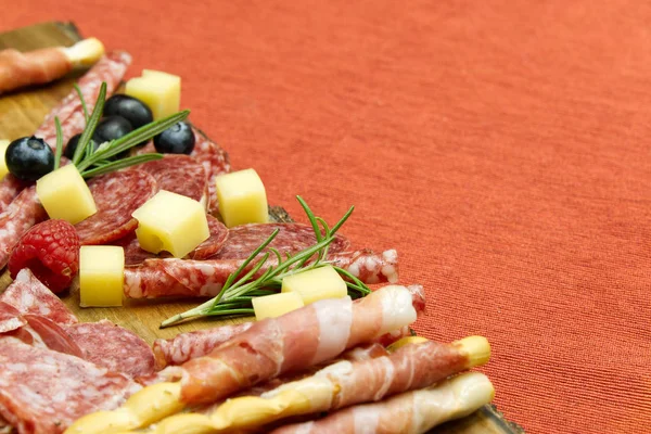 Snack antipasti de carne y queso con jamón Prosciutto, parmesano, queso azul, melón melón y aceitunas sobre tabla de servir de madera de olivo sobre fondo rojo — Foto de Stock