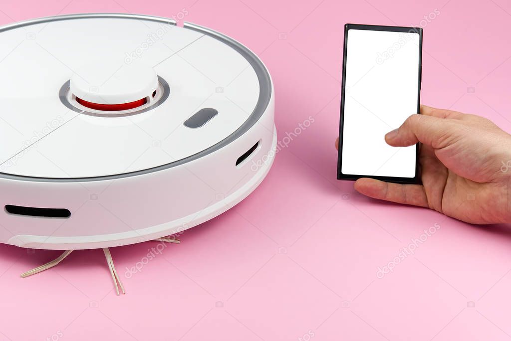 white Robotic vacuum cleaner isolated on pink background and hand holding smartphone with white screen, mockup