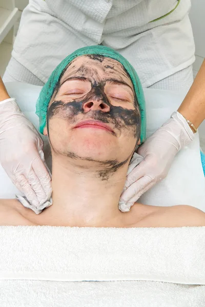 Schoonheidsspecialiste wast een natuurlijk hydraterend masker af op het gezicht van een jonge mooie vrouw. Zwart bamboe masker. Sluiten foto — Stockfoto