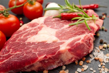 Baharatlı ve sebzeli çiğ biftek. Restoran yemeği için gerekli malzemeler. Taze et, tuz, biberiye, kekik, biber, kiraz domatesleri, siyah taşta sarımsak. Gıda arkaplanı.