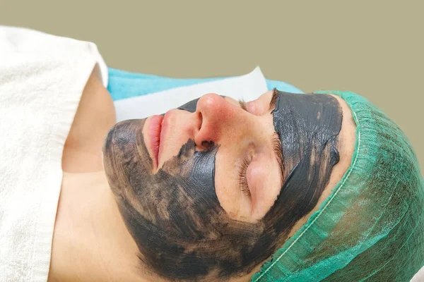 Молодая женщина в салоне красоты с черной маской на лице. Понятие косметологии. Косметолог проводит процедуру очищения лица проблемной кожей . — стоковое фото