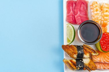Geleneksel Japon suşisi, mavi arka planda izole edilmiş beyaz bir tabakta. Lezzetli suşi, nigiri, sahimi ve maki seti. Lezzetli bir akşam yemeği ya da bir kişilik öğle yemeği. düz yat