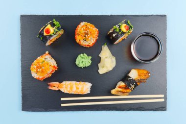 Geleneksel Japon suşisi seti siyah taşla servis edilir. Lezzetli suşi, nigiri, sahimi ve maki seti. Lezzetli bir akşam yemeği ya da bir kişilik öğle yemeği. düz mavi üzerine izole yatıyordu