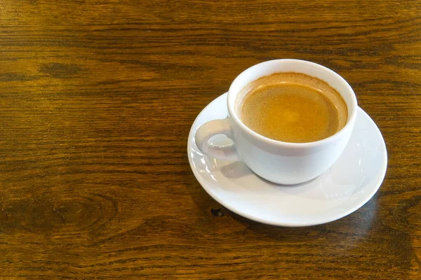 Filiżanka kawy na drewnianym stole w restauracji lub kawiarni. Biały widok na filiżankę ceramiki powyżej z miejsca kopiowania — Zdjęcie stockowe