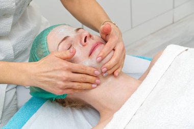 Güzellik uzmanı genç ve güzel bir kadının yüzüne doğal nemlendirici bir maske takar. Yaşlanma önleyici ve kırışıklık önleyici maske bir fırçayla yüze uygulanır. Kozmetoloji konsepti. Kozmetik uzmanı