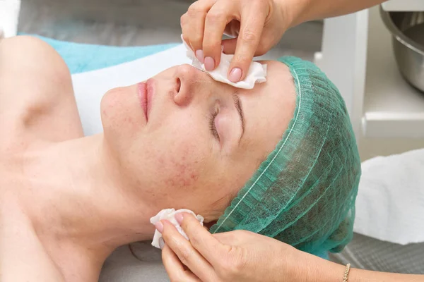 Beautician applies a natural moisturizing mask to the face of a young beautiful woman. Anti-aging mask and wrinkles for problem skin. Cosmetology concept. The cosmetologist performs the procedure to — Stock Photo, Image