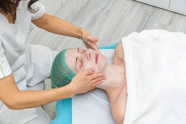 Mooie jonge vrouw met natuurlijke hydraterende masker op het gezicht. Schoonheidsbehandeling. Anti-aging huid en gelaatsrimpels. Cosmetologisch concept. De cosmetoloog voert de procedure uit om de — Stockfoto