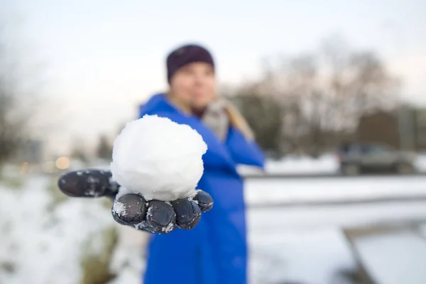 Una mano in un guanto di pelle nera tiene una palla di neve con uno sfondo di un campo innevato. la gioia dell'inverno e della neve, un popolare gioco di guerra della neve. focalizzazione morbida — Foto Stock