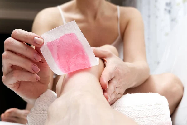 Mulher usando tiras de cera rosa. Mulher bonita fazendo depilação para as pernas com depilação, isolada em branco — Fotografia de Stock