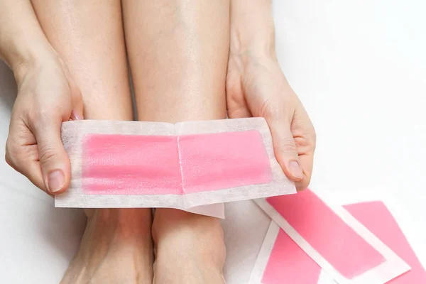 Woman using pink wax strips. Beautiful woman doing depilation for her legs with waxing, isolated on white