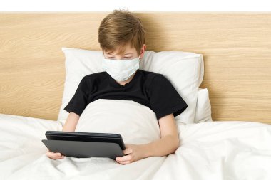 Evde karantinada çalışıyor, evde tabletle ders çalışan bir çocuk. Tıp maskeli çocuk tablet, sağlık hizmeti ve hasta çocuk konsepti, koronavirüs konsepti oynuyor..