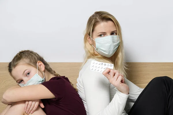 Daughter with mom in Surgical Masks. Family with kids in face mask ffp1. Virus and illness protection in public crowded place. Mother and daughter in bed room wear protection mask, health care and sick child, Protect Against Coronavirus concept.