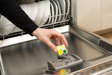 Bütünleşik bulaşık makinesini kapatıyoruz. Bulaşık makinesi dolu. Bulaşık makinesi tableti tutan kadın..