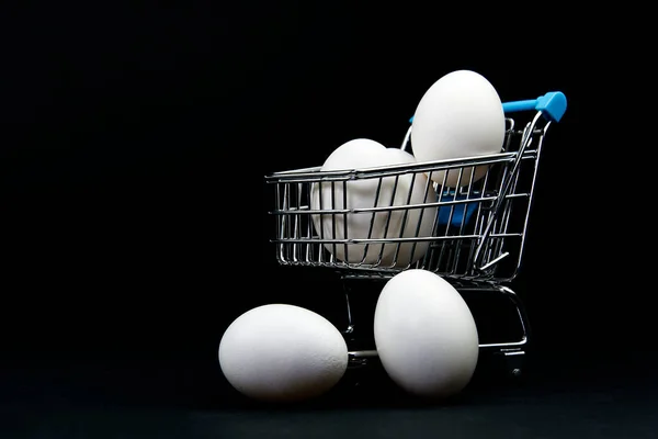 Ovos brancos de frango em um carrinho de compras. isolado em preto — Fotografia de Stock