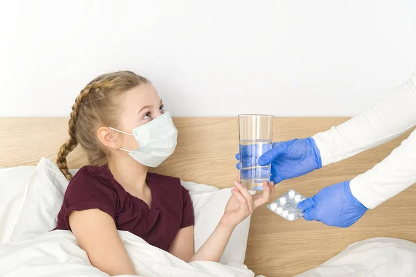 침대에 누워 있는 한 소녀에게 알약 과 물 한 컵을 준다. 바이러스에 감염되지 않도록 마스크를 쓴 여자. 바이러스 성 질병, 감기, 코로나 바이러스에 대한 격리와 치료의 개념 — 스톡 사진