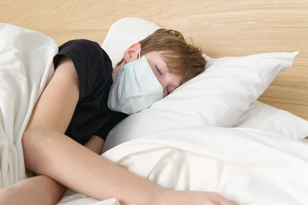 Un niño con una máscara de protección contra el virus duerme en la cama. niño en la habitación de la cama usar máscara de protección, cuidado de la salud y el concepto de niño enfermo o caronavirus — Foto de Stock