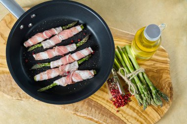 Kızartma tavasında kuşkonmaz etrafında lezzetli pastırma. Tahtada pişmeye hazır taze kuşkonmaz. Sağlıklı yemek tarifleri kavramı