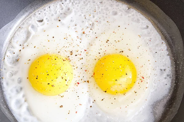 Huevos fritos con especias en la sartén negra de cerca. dos huevos —  Fotos de Stock